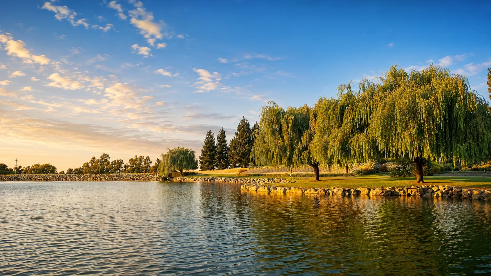 The private lake in low golden light, willows along the far bank above the rock-edged shore